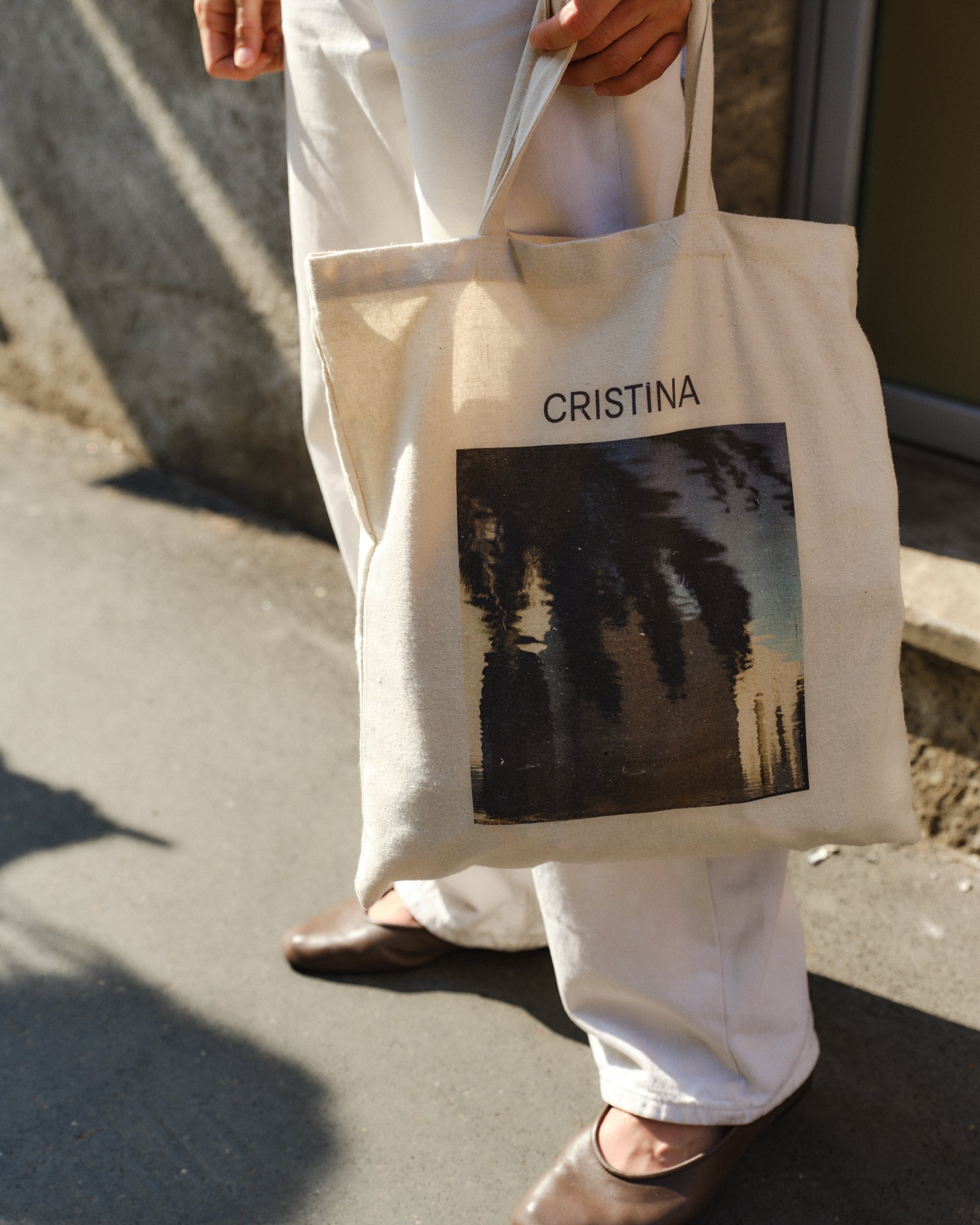 A closeup of a tote bag printed with a dreamy photo of a palm tree and the CRISTINA logo