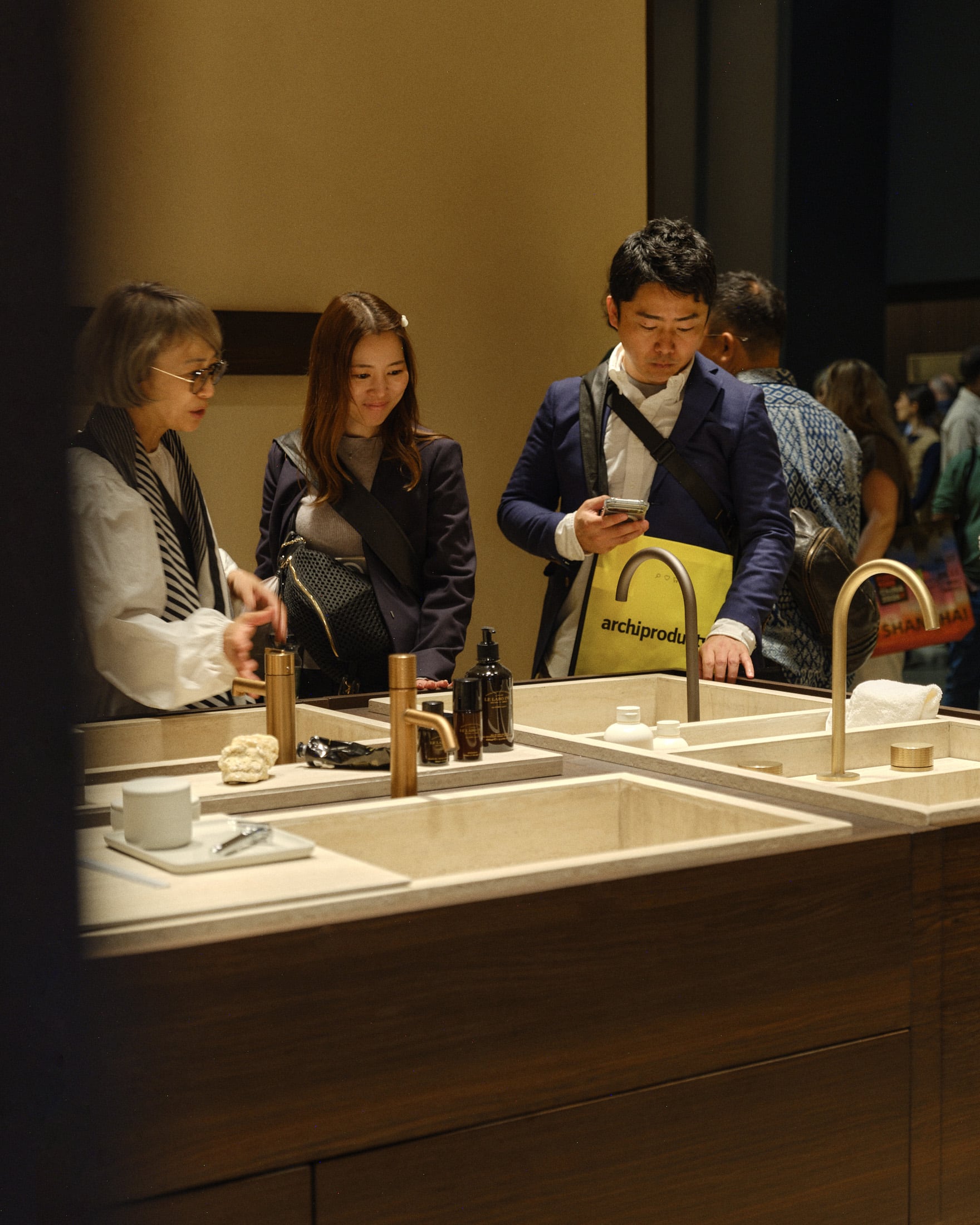 Group of fair visitors examine a set of bathroom taps mounted to a big table